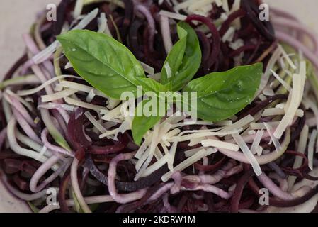 Gesunde Nachbildung von Nudeln mit spiralförmigen Zucchini, verziert mit Basilikumblättern, garniert mit Parmesankäse und schwarzem Pfeffer, Nahaufnahme Stockfoto