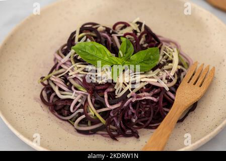 Gesunde Imitationsnudeln aus spiralförmigen Zucchini, verziert mit Basilikumblättern und garniert mit Parmesankäse und schwarzem Pfeffer auf Bambuspl Stockfoto