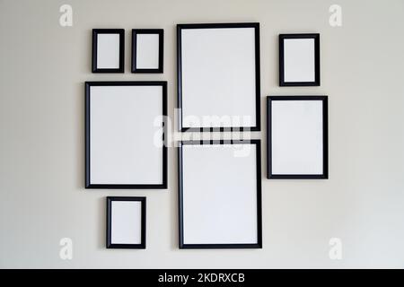 An der grauen Wand hängen gerahmte Fotos unterschiedlicher Größe. Modell. Stockfoto