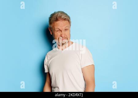 Porträt eines reifen Mannes in weißem T-Shirt, isoliert auf blauem Studiohintergrund. Sich krank fühlen. Saures Gesicht Stockfoto