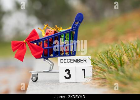 Der 31. Dezember steht auf einem Holzteller im Kalender, und daneben ist ein Karren aus einem Supermarkt mit Geschenken auf der Straße, glückliches neues Jahr, neues Ye Stockfoto