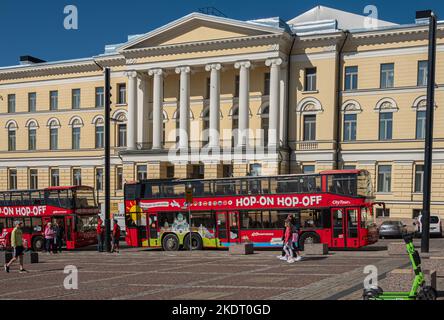 Helsinki, Finnland - 19. Juli 2022: Hop-on Hop-off-Busse auf dem Senatsplatz vor dem gelben Oikeuskanzerslerinvirasto, dem historischen Regierungsexekuter Stockfoto