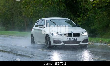 Weißes Fahrzeug der BMW 1 Serie 2017, das im Regen auf nasser Straße fährt Stockfoto