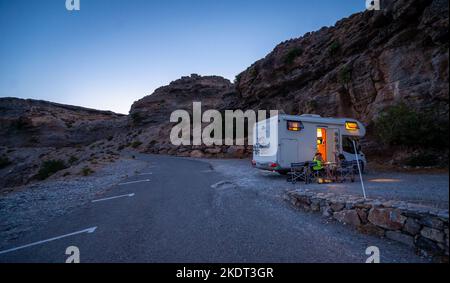 Wohnmobil-Wohnmobil am Strand unter einer Klippe, Kreta, Griechenland geparkt. Familie, die mit dem Wohnmobil unterwegs ist und am Strand zu Abend isst. Reisende mit Wohnmobil sind Camping Stockfoto