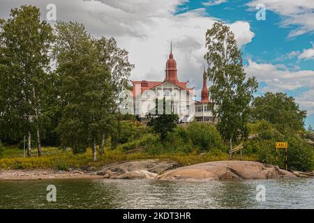 Helsinki, Finnland - 19. Juli 2022: Restaurant Saaristo mit rotem Dach auf seiner eigenen grünen Insel unter blauer Wolkenlandschaft am Eingang zum Hafen von Helsinki. Stockfoto