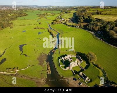 Luftaufnahme von Trittsteinen über einen kleinen Fluss, der zu den Ruinen einer alten Burg führt (Ogmore Castle, Glamorgan, Wales) Stockfoto