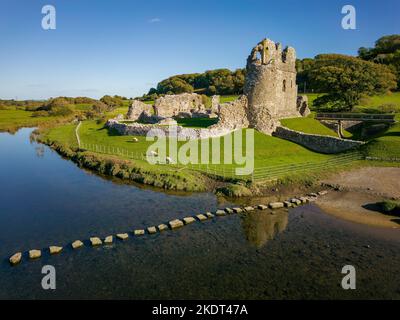 Luftaufnahme von Trittsteinen über einen kleinen Fluss, der zu den Ruinen einer alten Burg führt (Ogmore Castle, Glamorgan, Wales) Stockfoto