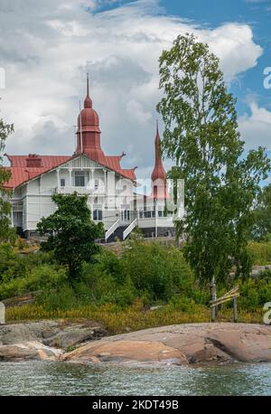 Helsinki, Finnland - 19. Juli 2022: Portrait, Red Roofed Restaurant Saaristo auf seiner eigenen grünen klippan Insel unter blauer Wolkenlandschaft. Stockfoto