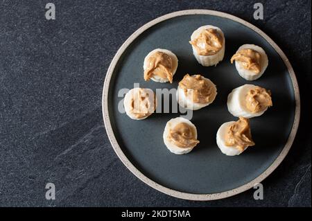 Banane mit Erdnussbutter - gesunder Snack isoliert auf dunklem Hintergrund von oben Stockfoto