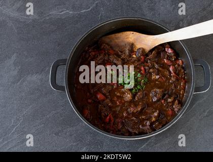 Topf mit frisch gekochtem scharfem Rindfleischeintopf, isoliert auf dunklem Hintergrund von oben mit Kopierbereich Stockfoto