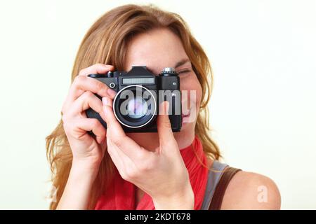 Junge Rothaarige, die mit einer alten Spiegelreflexkamera von 35mm durch den Sucher schaut. Stockfoto