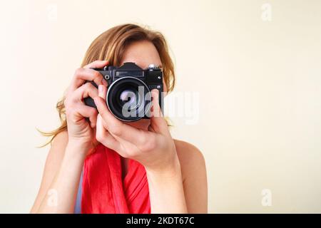 Junge Rothaarige, die mit einer alten Spiegelreflexkamera von 35mm durch den Sucher schaut. Stockfoto