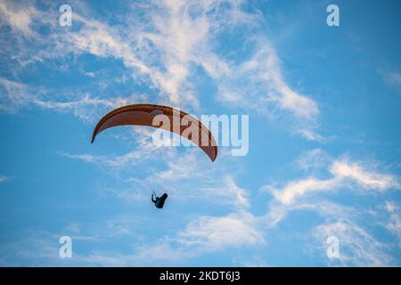 Gleitschirm, der unter dem blauen Himmel vor dem Hintergrund von Wolken fliegt Stockfoto