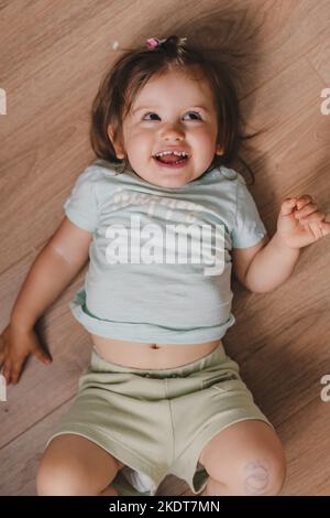 Kleinkind Baby Kleinkind in T-Shirt auf Parkett liegend und Blick nach unten, Draufsicht. Wunderschönes Porträt. Hautpflege. Lächelndes, glückliches Kind. Stockfoto