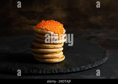 Roter Kaviar auf kleinen Pfannkuchen Blinis mit saurer Creme auf dunklem Hintergrund Stockfoto