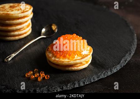 Roter Kaviar auf kleinen Pfannkuchen blinis mit saurer Creme und einem Löffel auf einem Schiefer Stockfoto