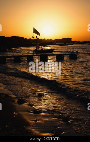 Fischerboote und Pier in der untergehenden Sonne im Ferienort Roda auf der Insel Korfu im Ionischen Meer in Griechenland. Stockfoto