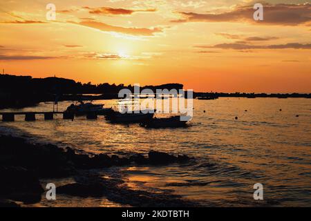 Fischerboote und Pier in der untergehenden Sonne im Ferienort Roda auf der Insel Korfu im Ionischen Meer in Griechenland. Stockfoto