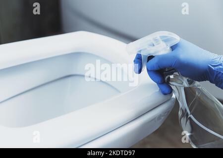 Nahaufnahme von Handschuhen in blauen Gummischutzhandschuhen. Hausfrau Reinigung Toilettenschüssel, Sitz mit Waschmittel Flüssigkeit im Bad oder Toilette. Desinfektion, Hygiene, Reinigungsdienstkonzept Stockfoto
