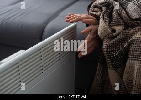 Frau, die sich in Innenräumen in der Nähe des Heizelements die Hände wärmte, Nahaufnahme Stockfoto