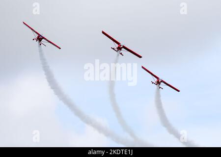 Drei kleine rote Sportflugzeuge mit Rauchstreifen machen während einer Flugshow einen Parallelflug Stockfoto
