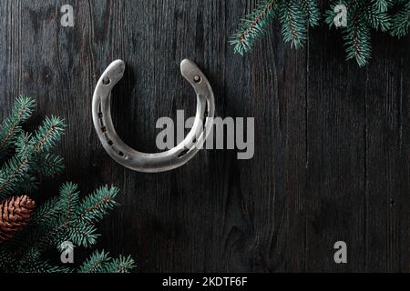 Alte Hufeisen- und Fichtenzweige auf schwarzem Holzgrund. Speicherplatz kopieren. Stockfoto