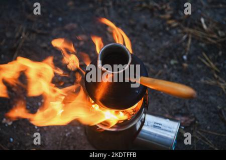 Nahaufnahme Kaffee in türkischem Cezve auf Campingkocher. Tragbarer Herd, der Holzspäne verbrannte. Draufsicht. Stockfoto