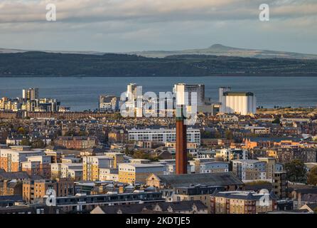 Blick über die Dächer auf den Firth of Forth mit einem industriellen Schornsteinturm und Hochhäusern. Edinburgh, Schottland, Großbritannien Stockfoto