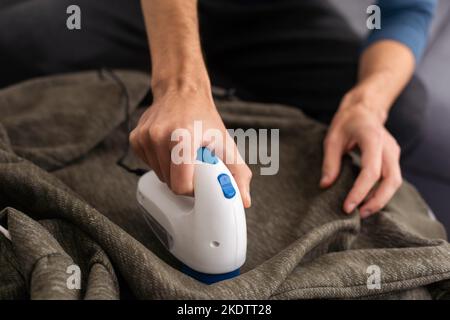 Kabelloses Gerät zum Reinigen von Strickstoffen von Flusen. Der Mann entfernt die Flusen vom Pullover. Stockfoto