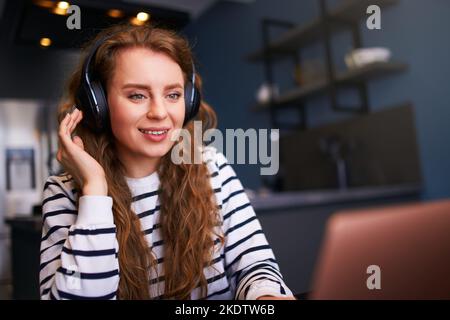 Customer Support Service Call Center Manager spricht, arbeitet von zu Hause aus. Lockige Frau mit Headset, spricht auf einer Videokonferenz mit einer Webcam am Laptop. Jung Stockfoto