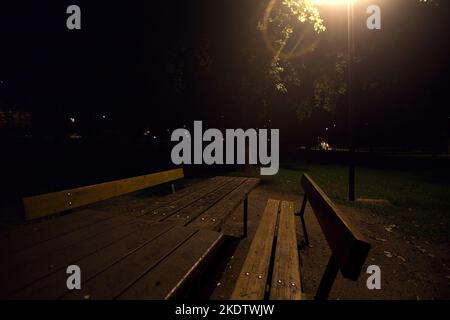 Holzbank in einem Park unter einer Straßenbeleuchtung in der Nacht Stockfoto