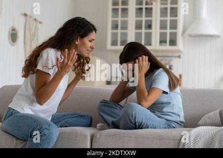 Verängstigtes Teenager-Mädchen, das Ohren bedeckt und den Schreien der Mutter zuhört, das kastisierende Kind sitzt auf dem Sofa Stockfoto