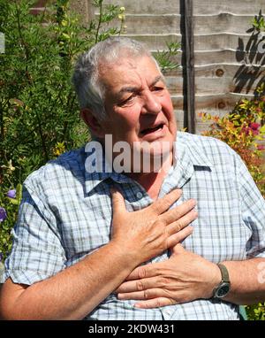 Älterer oder älterer Mann, der seine Brust in Schmerzen hält. Möglicherweise Verdauungsstörungen oder Herzinfarkt. Stockfoto