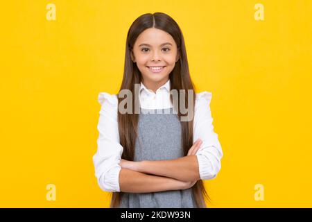 Glückliches Mädchengesicht, positive und lächelnde Emotionen. Selbstbewusstes Kind: Arme gekreuzt halten, isoliert auf gelbem Hintergrund, leerer Raum. Kleiner Kaukasier Stockfoto