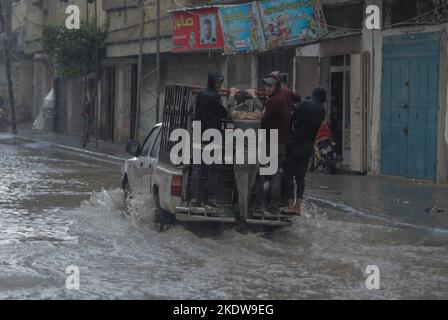 Palästinenser steigen auf einem Lastwagen entlang der Straße des Flüchtlingslagers Jabalia, inmitten des starken Regens im nördlichen Gazastreifen. Stockfoto