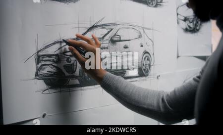 afroamerikanischer Designer aus dem Automobilbereich zeichnet Skizzenvorlage mit Marker auf dem Whiteboard und entwickelt futuristisches Design für Elektroautos. Er arbeitet in der Auto-Design-Entwicklung modernes Studio. Stockfoto