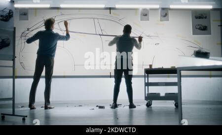 Zwei verschiedene männliche Automobildesigner zeichnen gemeinsam eine Skizze mit Marker auf Whiteboards und entwickeln so ein Design der neuen Generation von Elektroautos. Sie arbeiten in einem modernen Entwicklungsstudio für Fahrzeugdesign. Stockfoto