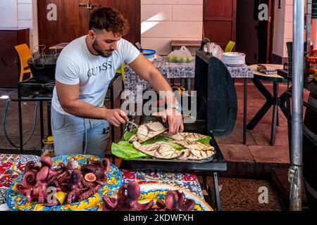 Ein junger Mann kocht Fisch auf Einem Grill auf dem Ballaro Street Market, Palermo, Sizilien, Italien. Stockfoto