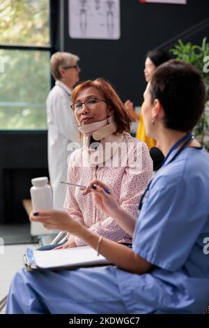 Leitender Patient mit Halsband, der einen medizinischen Termin im Wartebereich des Krankenhauses hat. Spezialist hält Pillen Flaschen erklären Medikamente Rezept. Unterstützung der Medizin Stockfoto