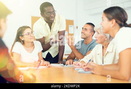 Freundliche afroamerikanische Englischlehrerin, die Sprachkurse für eine Gruppe von Erwachsenen gibt Stockfoto