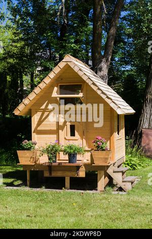 Spielhaus-Fassade aus Kiefernholz für Kinder mit blühenden Pflanzen auf der Veranda und Dach aus Zedernholz im Sommer. Stockfoto