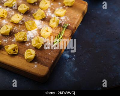 Nahaufnahme. Rohe hausgemachte Knödel auf einem Schneidebrett mit Mehl bestreut. Dunkelblauer Marmorhintergrund. Kochen hausgemachte Knödel gefüllt mit Hackfleisch Stockfoto