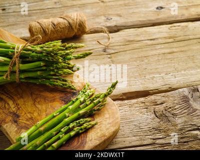 Grüne Spargeltriebe auf einem hölzernen Schneidebrett auf einem hölzernen Hintergrund. Nützliches Vitamin-Produkt, gebrauchsfertig. Zutat für verschiedene Gerichte. Stockfoto