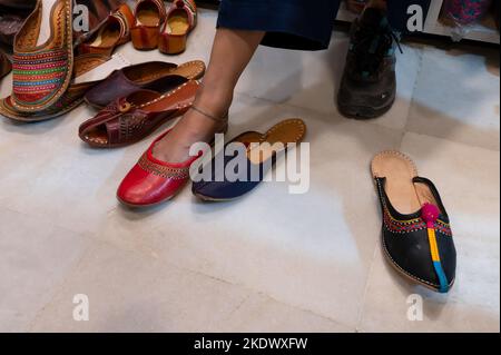 Schöne indische Frau, die ihren Fuß für das Anbringen von bunten Rajsathani Damenschuhen im Schuhgeschäft am berühmten Sardar Market und Ghanta Ghar Clock probiert Stockfoto