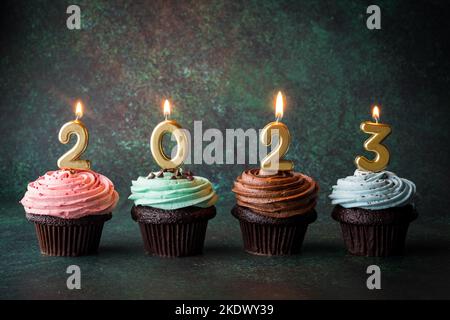 Cupcakes mit golden beleuchteten Zahlenkerzen für das neue Jahr 2023. Stockfoto