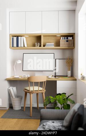 Minimaler nordisch-skandinavischer Arbeitsraum mit PC-Desktop-Computer auf Holztisch, Holzstuhl, Hauspflanzen, Sofa, weißen Einbauregalen und Stockfoto