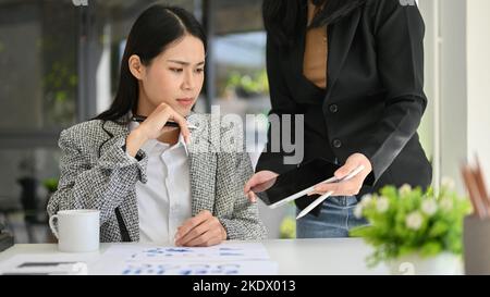 Professionelle und gestresste Millennial Asian Businesswoman oder weibliche Manager arbeiten mit ihrer Sekretärin oder Assistentin, Überprüfung ihrer Projektdetails auf ta Stockfoto