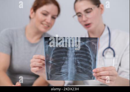 Der Arzt konsultiert eine kaukasische Frau und kommentiert die Röntgenaufnahme der Lunge. Stockfoto