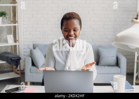 Glückliche, schöne afroamerikanische Freiberuflerin, die per Videoanruf mit Kollegen online spricht. Frau mit Online-Webkonferenz Stockfoto