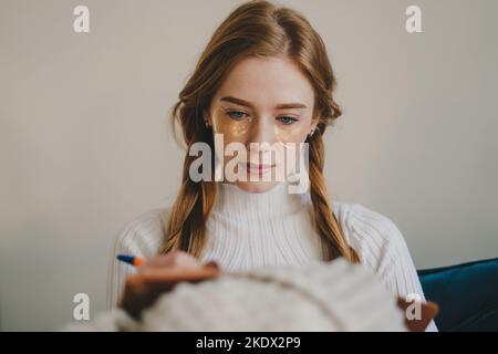 Schöne junge Frau mit unter den Augen Flecken halten Stift mit Notebook und sitzt auf dem Sofa im Home Office. Bildungskonzept. Erholsame Zeit. Stockfoto